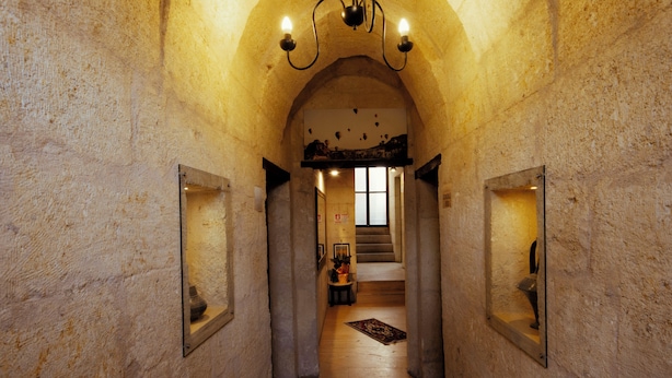 A hallway with stone walls, a wooden floor, and a chandelier. There are framed pictures on the walls and a rug on the floor. - Tafana Cave & Stone Lodge (Ürgüp)