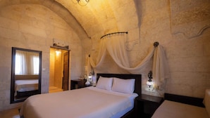 A bedroom with a large bed, a mirror, a nightstand with a lamp, and a stone wall. - Tafana Cave & Stone Lodge (Ürgüp)