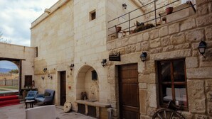 A stone building with a reception sign, outdoor seating, and a large wooden wheel. - Tafana Cave & Stone Lodge (Ürgüp)