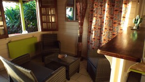A room with wicker furniture, a window with shutters, a mirror, and patterned curtains.