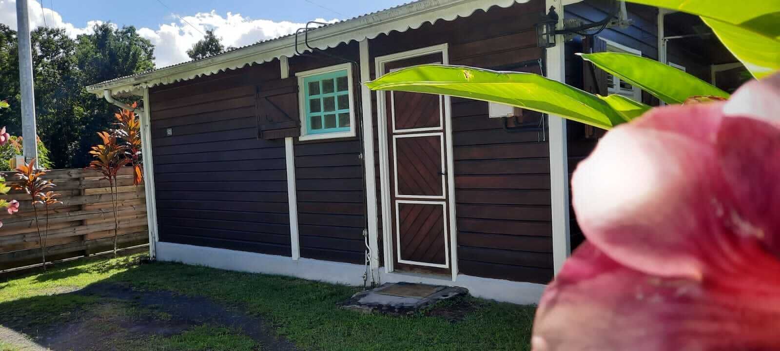 A small wooden house with a dark exterior and white trim, a single window, and a door.