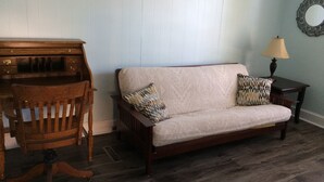 Ein Zimmer mit einem Holztisch, einer Couch mit gemusterten Kissen, einem kleinen Tisch mit einer Lampe und einem Spiegel an der Wand.