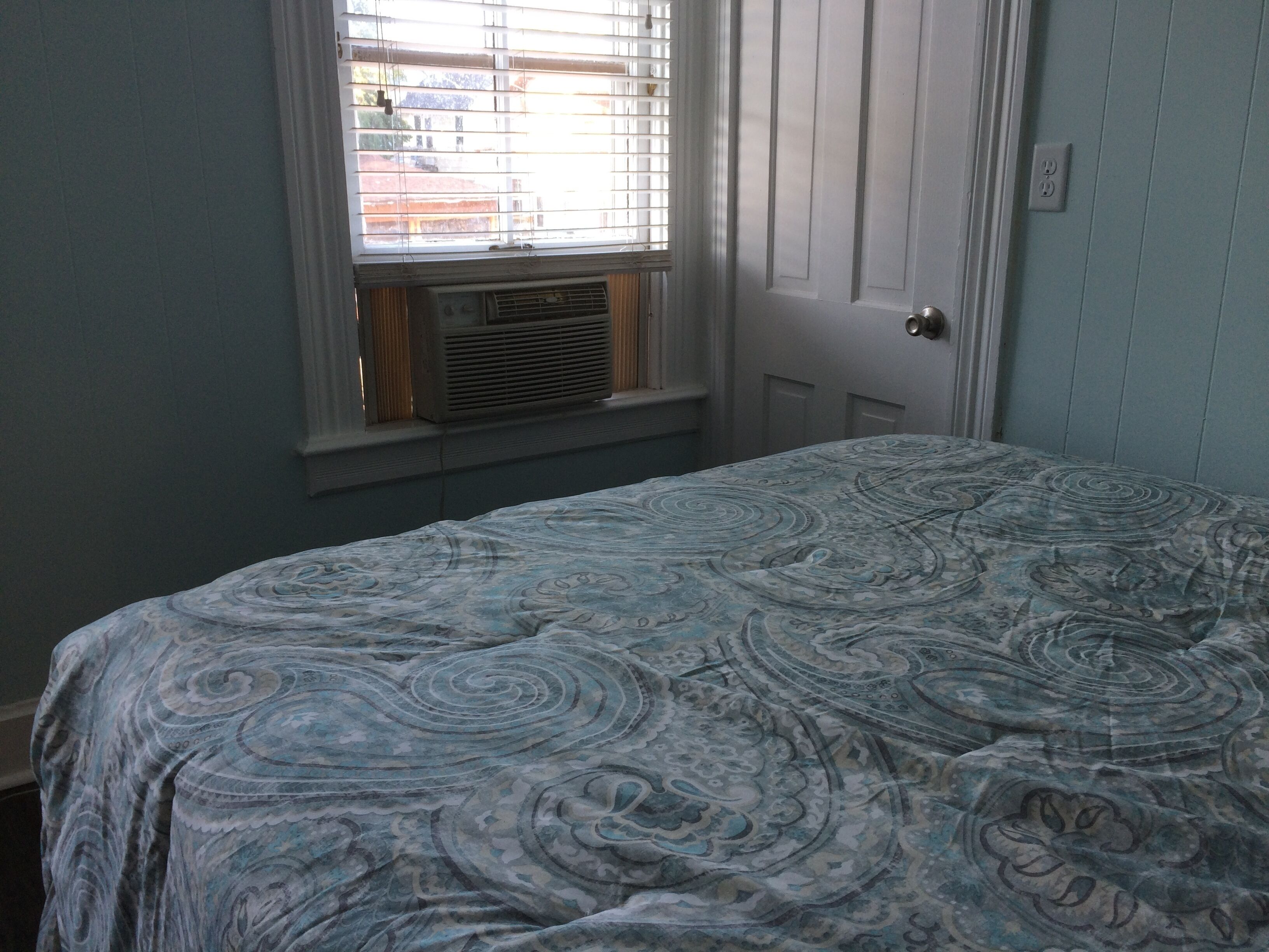 A bedroom with a bed, a window with blinds, and a door.