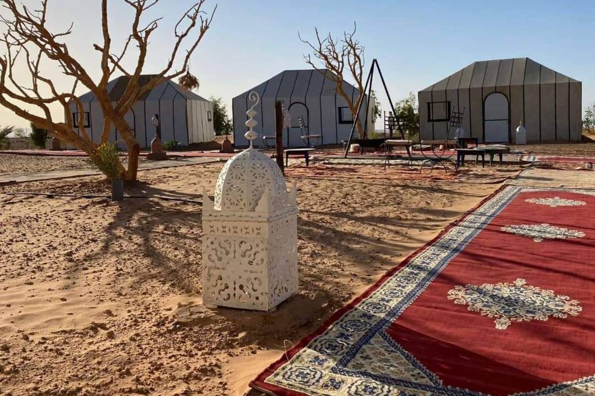 A desert landscape with three modern, dome-shaped buildings, a white decorative structure, and a patterned red carpet.