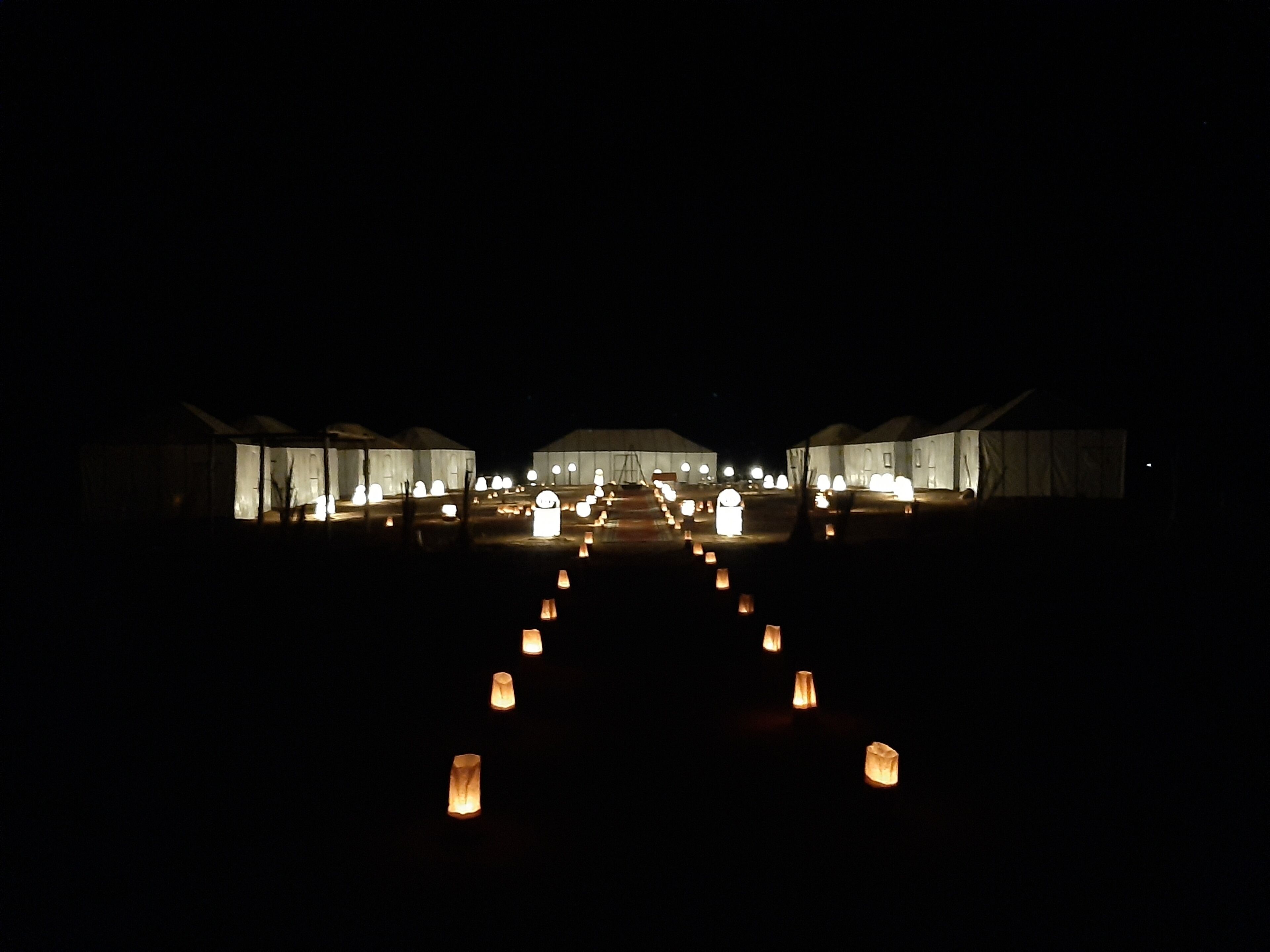 A series of tents with a central building, connected by a pathway lined with lanterns.