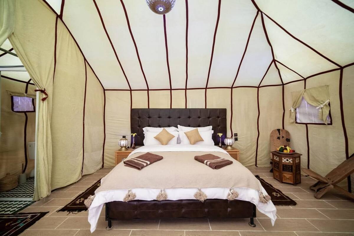 A tent-style room with a large bed, bedside tables, a television, and a small cabinet.