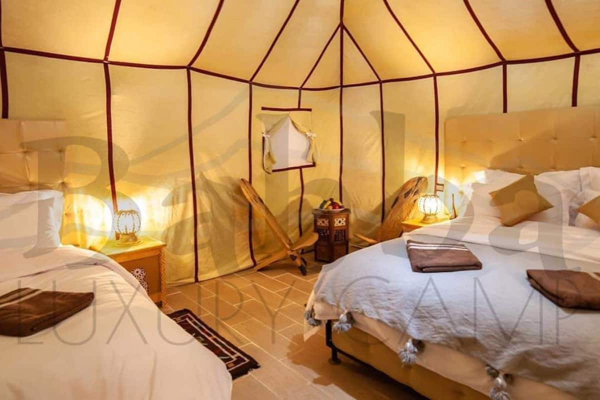 A tent-style room with two beds, wooden furniture, and warm lighting.