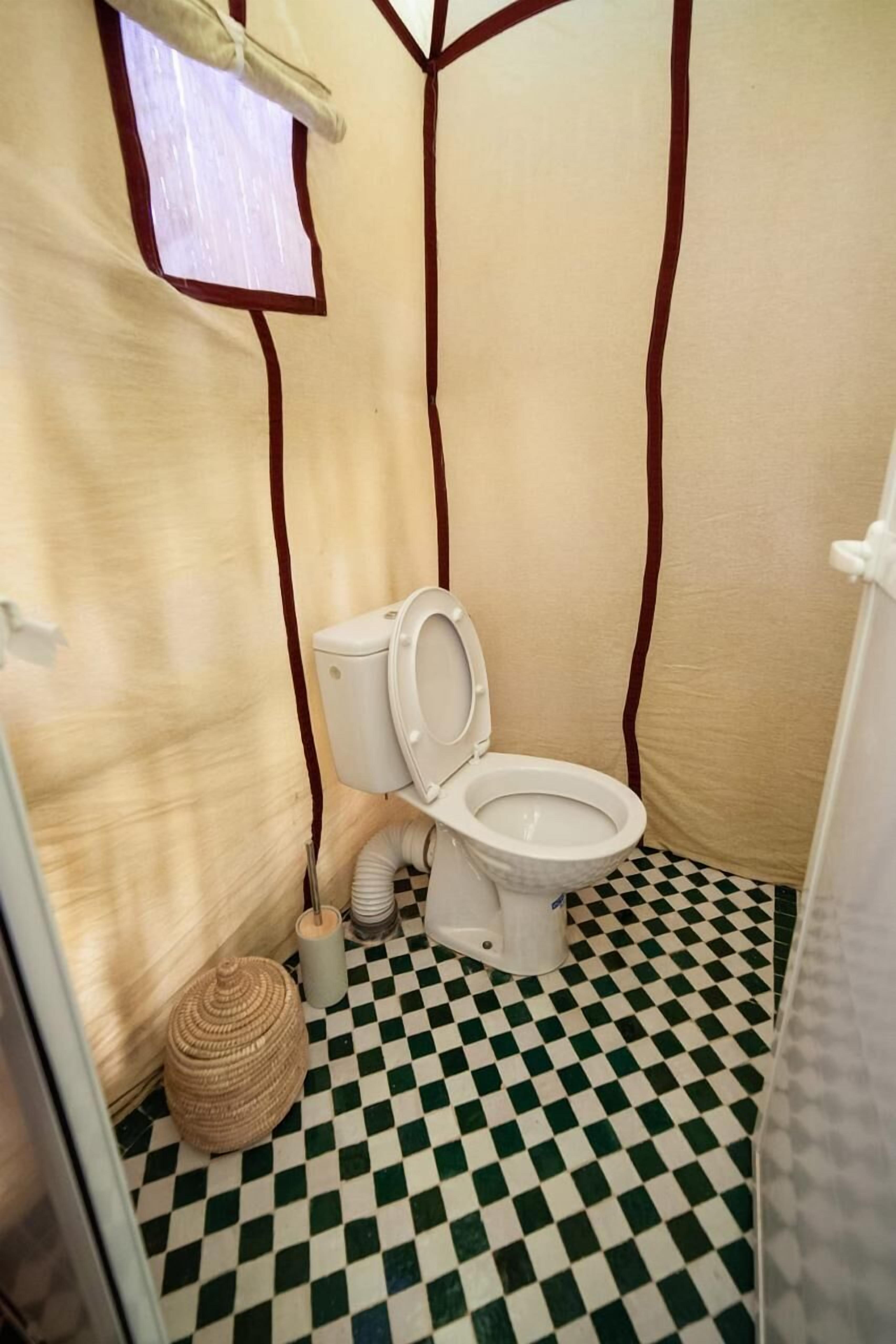 A small bathroom with a white toilet, a checkered floor, and a window with a view of the outside.