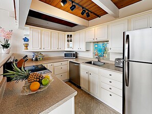 A modern kitchen with white cabinets, stainless steel appliances, and a wooden ceiling.
