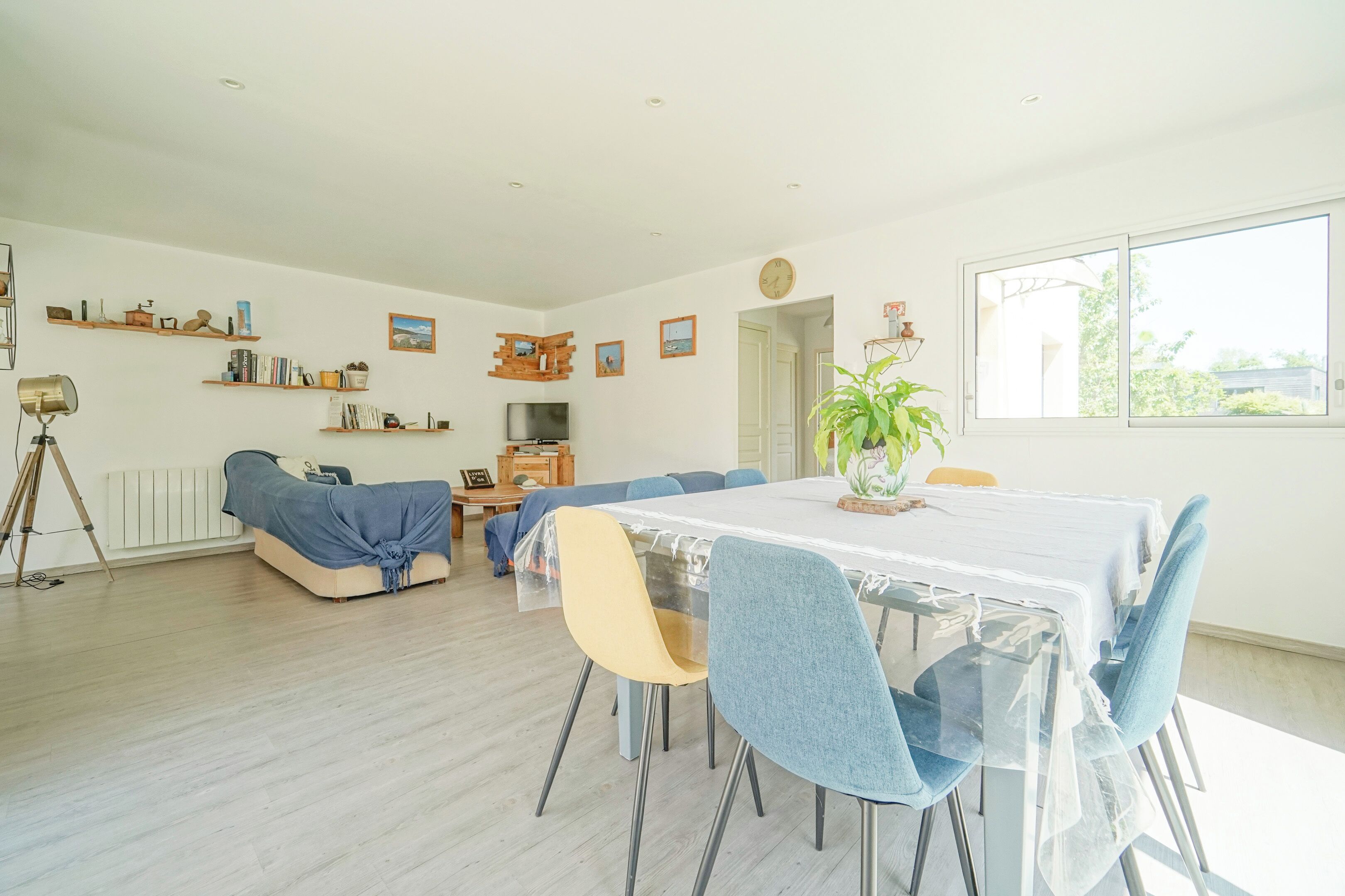 Een ruime woonkamer met een eethoek, een bank, een televisie en een groot raam.