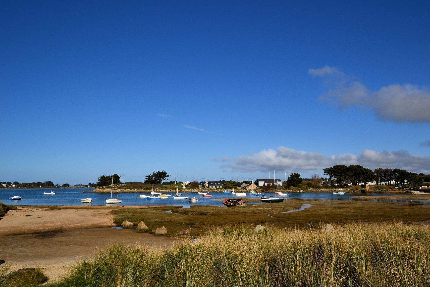 Un paysage côtier avec des bateaux amarrés près du rivage, une plage de sable et des zones herbeuses.