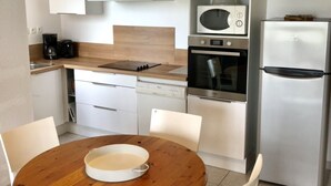 Une cuisine compacte avec des meubles blancs, un four à micro-ondes, un four et un réfrigérateur. On y trouve une table à manger en bois avec des chaises.