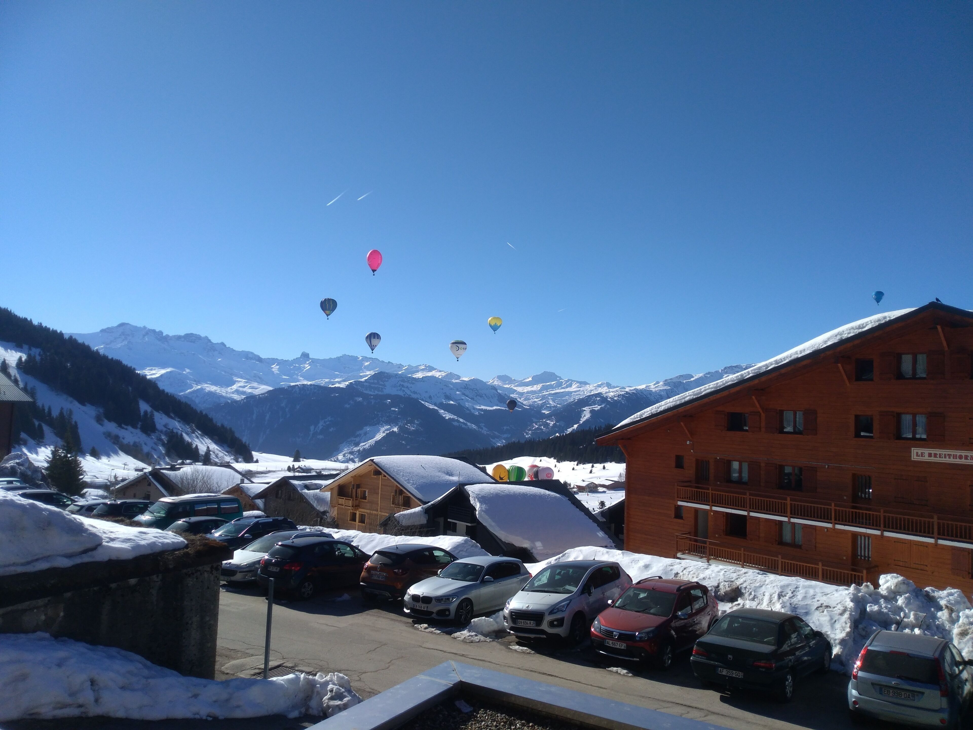 Um hotel com vista para montanhas cobertas de neve e carros estacionados em primeiro plano.