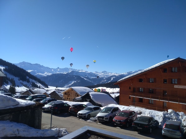 A hotel with a view of snow-covered mountains and parked cars in the foreground.