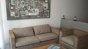 Una sala de estar con un sofá color beige, un sillón de mimbre y una mesa de centro de madera.