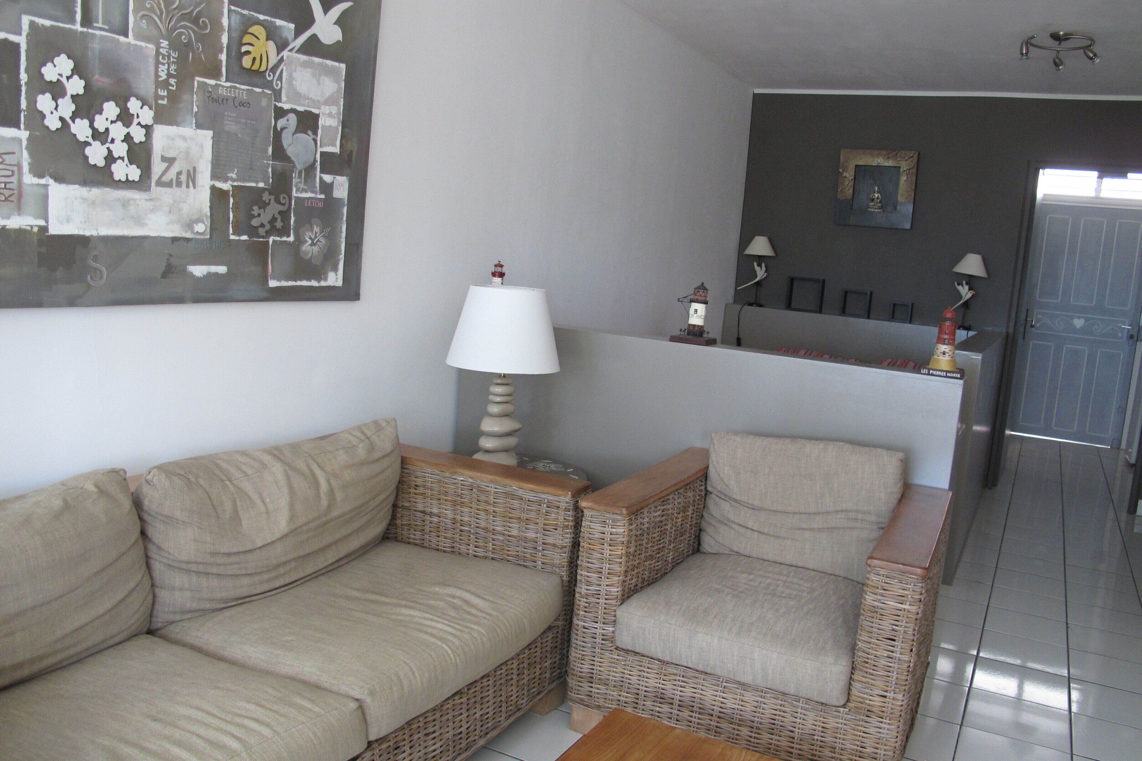 A living room with a beige sofa and two wicker armchairs, a white lamp, and a wall art piece.