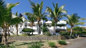 Un edificio blanco con varios balcones, rodeado de palmeras y un muro de piedra.