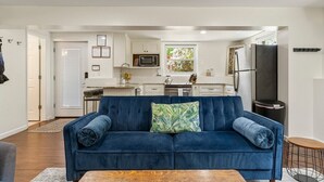 Un salon moderne avec un canapé bleu, une table basse en bois et une cuisine en arrière-plan.
