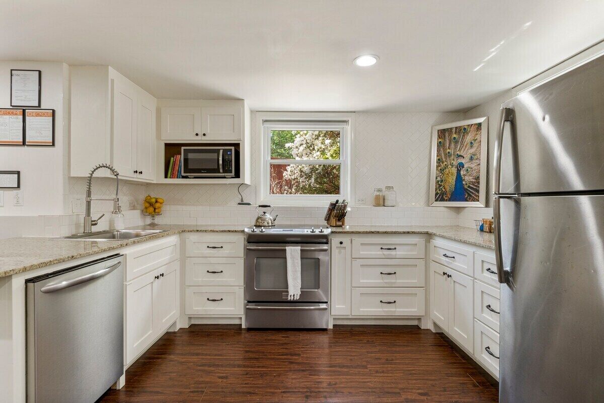 A kitchen with white cabinets, stainless steel appliances, a microwave, and a window with a view of trees.