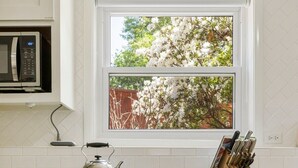 Une cuisine avec des meubles blancs, une cuisinière en acier inoxydable, une bouilloire et une fenêtre donnant sur les arbres.