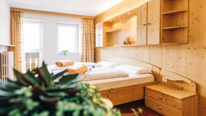 Ein Schlafzimmer mit Holzboden, einem Bett, einem Nachttisch, einer Kommode und einem Fenster mit Vorhängen.