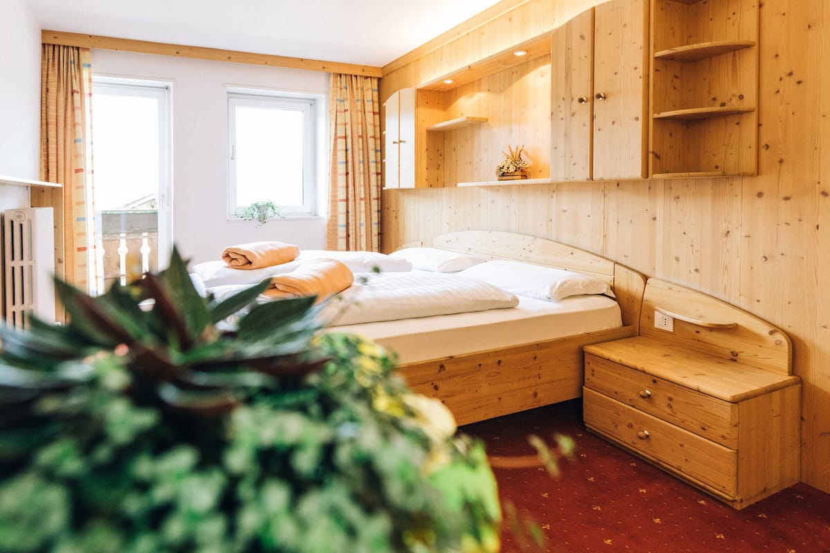 A wooden bedroom with a bed, a nightstand, a dresser, and a window with curtains.