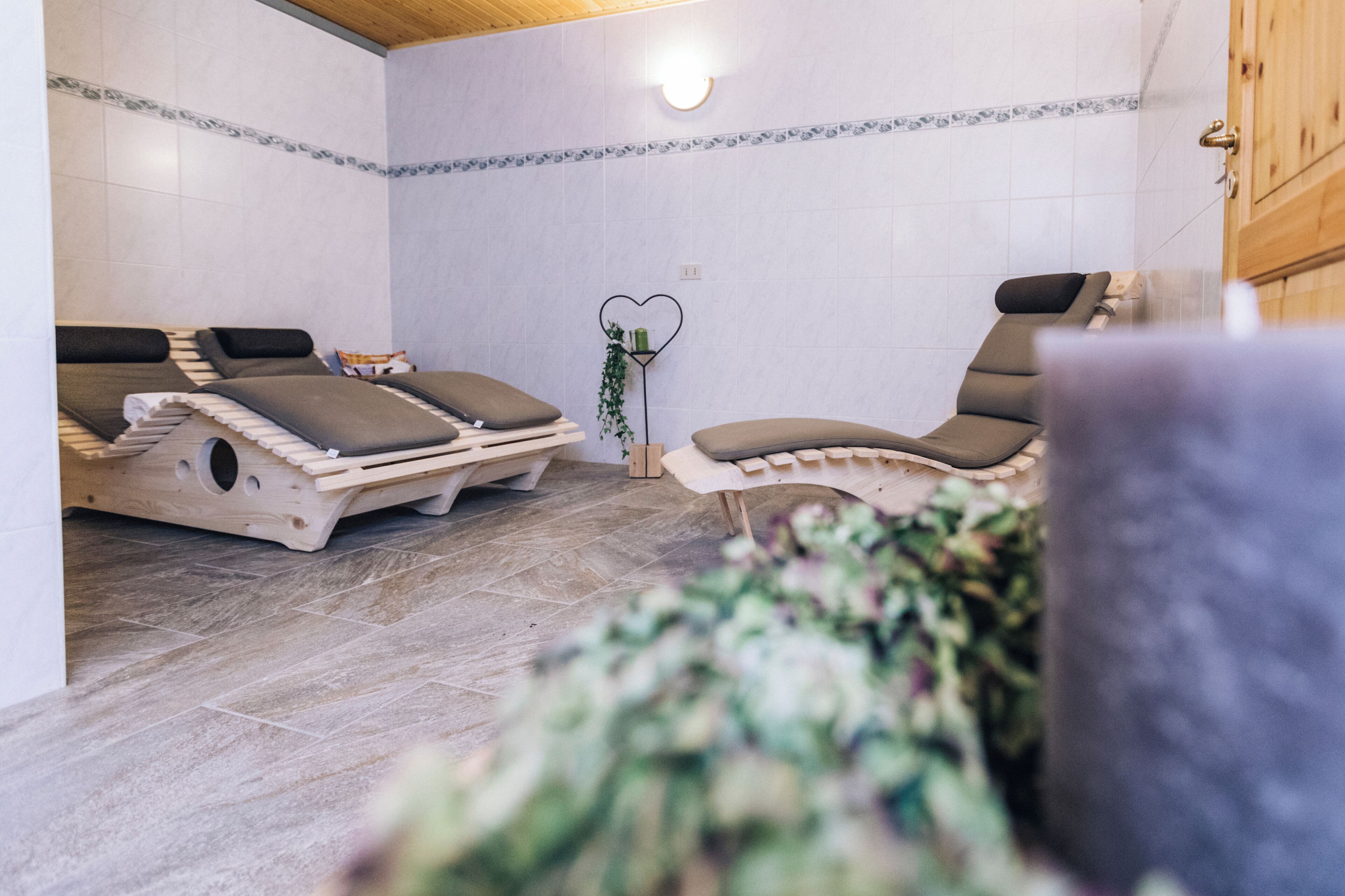 Una stanza spa con due lettini di legno, una pianta a forma di cuore e un muro rivestito di piastrelle.