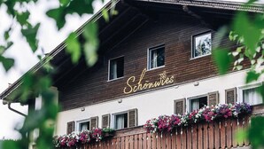 Ein hölzernes Gebäude mit einem Balkon, der mit Blumen geschmückt ist, und einem Schild mit der Aufschrift "Schönwies".