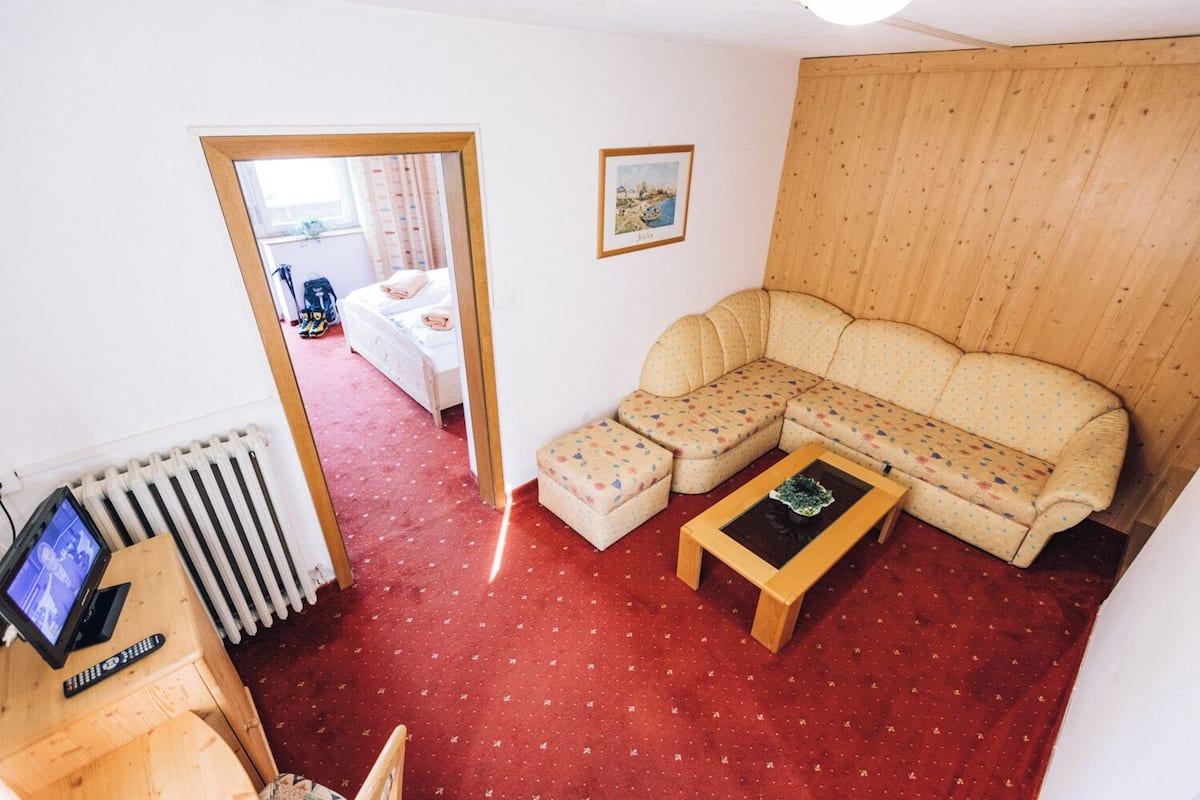 A room with a sofa, ottoman, and a small table. There is a radiator, a TV, and a picture on the wall.