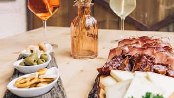 A wooden table with a charcuterie board, olives, crackers, and two glasses of wine.