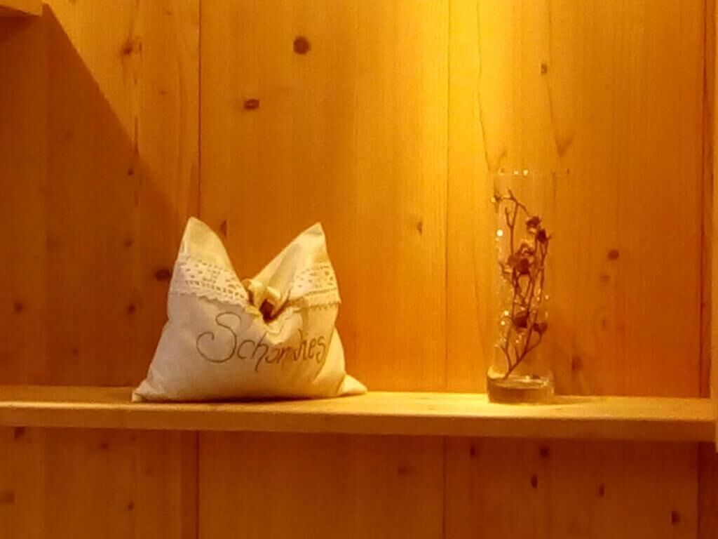 A wooden shelf with a white pillow labeled "Schmores" and a clear vase with dried flowers.