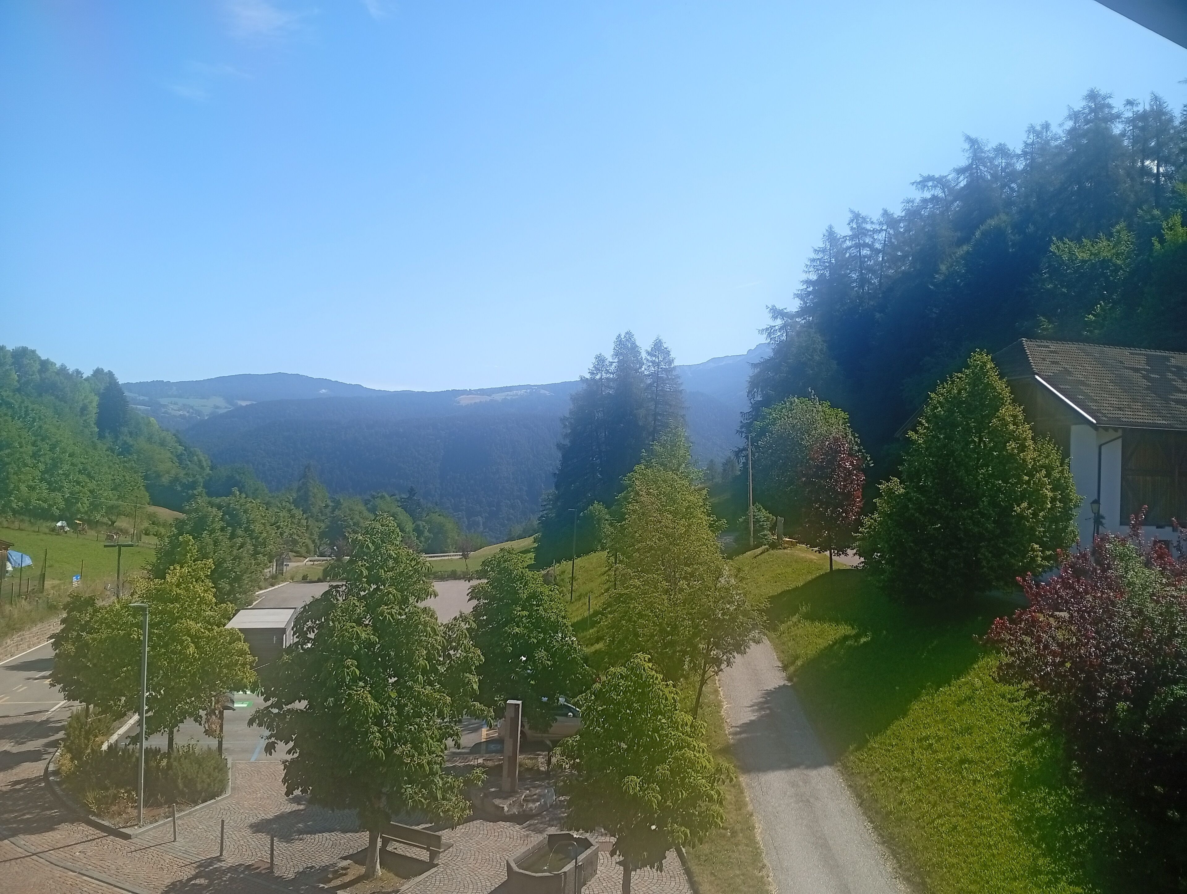 A rural landscape with a paved path, trees, and a small building.