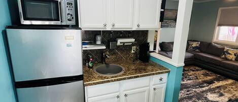 A compact kitchen with white cabinets, a stainless steel refrigerator, a microwave, and a granite countertop.