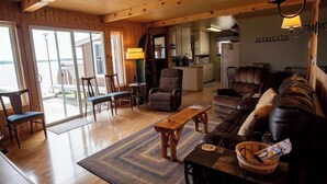 A cozy living room with a sofa, chairs, a wooden coffee table, and a kitchen in the background.