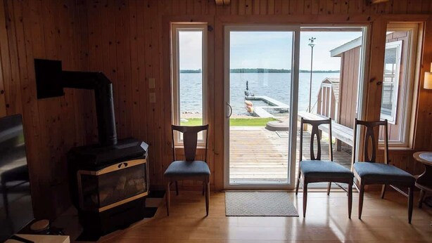 A cabin with a wood-burning stove, a sliding glass door to a deck, and a view of the water.
