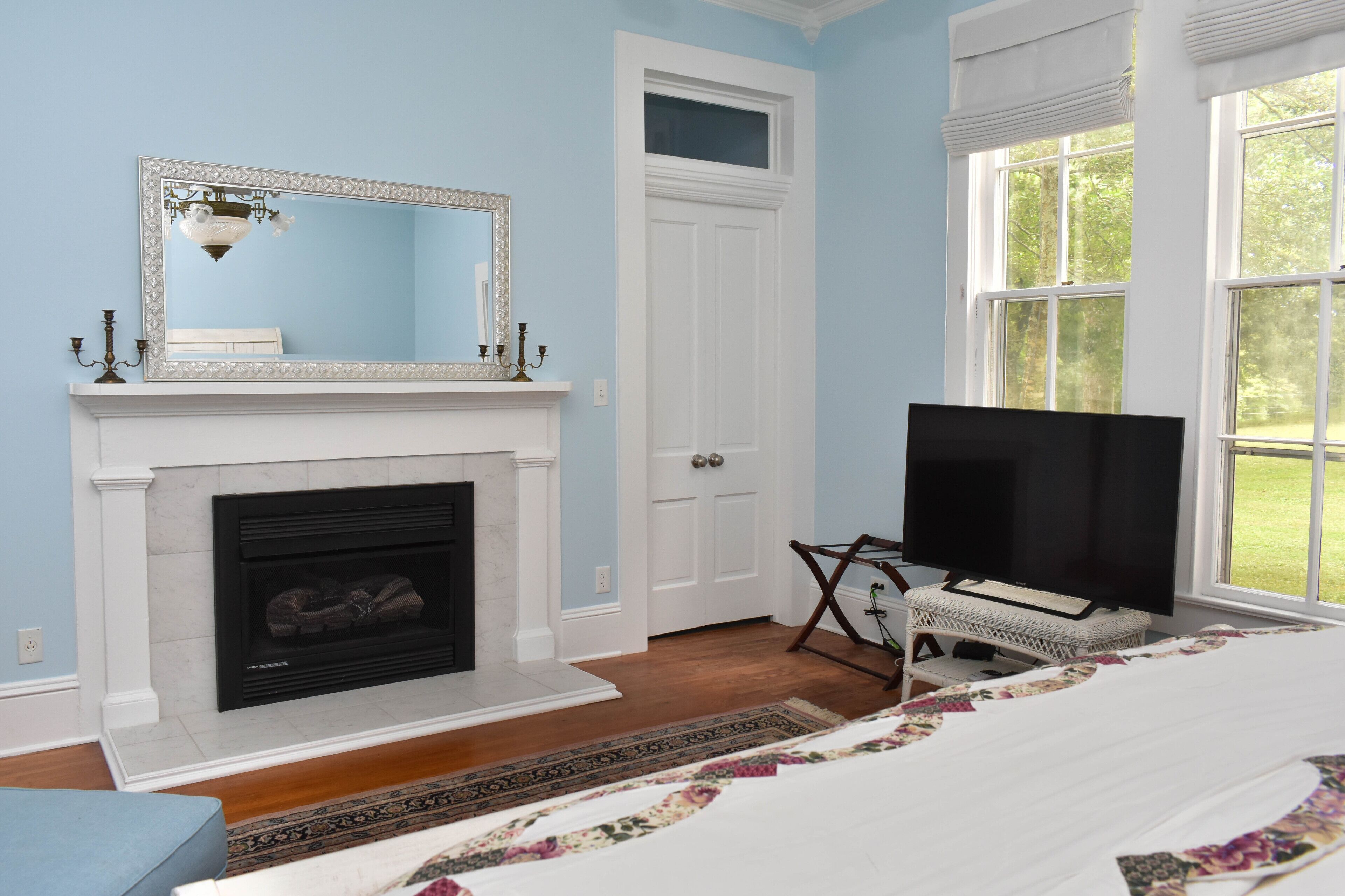 A bedroom with a fireplace, a television, and a large window.