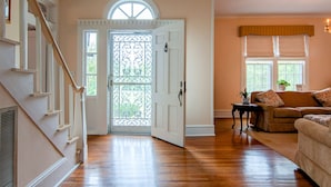 A spacious living room with hardwood flooring, a staircase, a white door with a decorative glass panel, and a cozy seating area with a sofa and a side table.