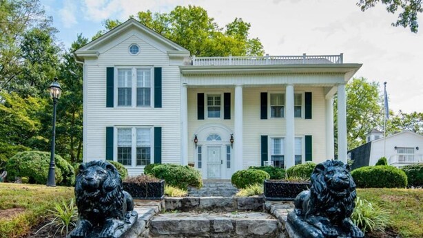 A two-story house with a front porch, stone steps, and two lion statues.