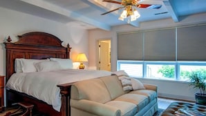 A bedroom with a wooden bed, a beige sofa, a ceiling fan, and a window with blinds.
