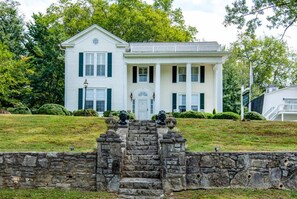 A two-story white house with a front porch, stone steps, and a small garden.