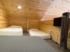 Una habitación con dos camas, un televisor montado en la pared y un calentador portátil.