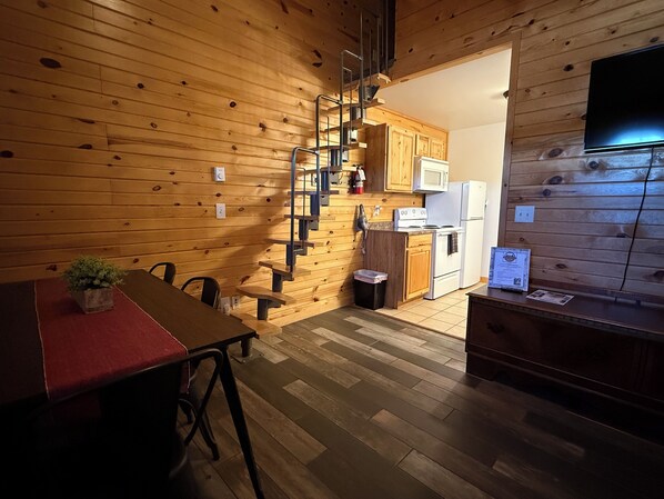 A wooden interior with a dining area, kitchen, and a staircase. - Frenchy's Hideaways Cabin #4 (Custer)