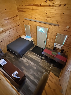 Een houten kamer met een bed, een bureau, een stoel en een deur.