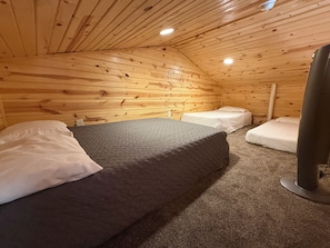 Una habitación tipo cabaña acogedora, con techo inclinado, paredes de madera y tres camas.