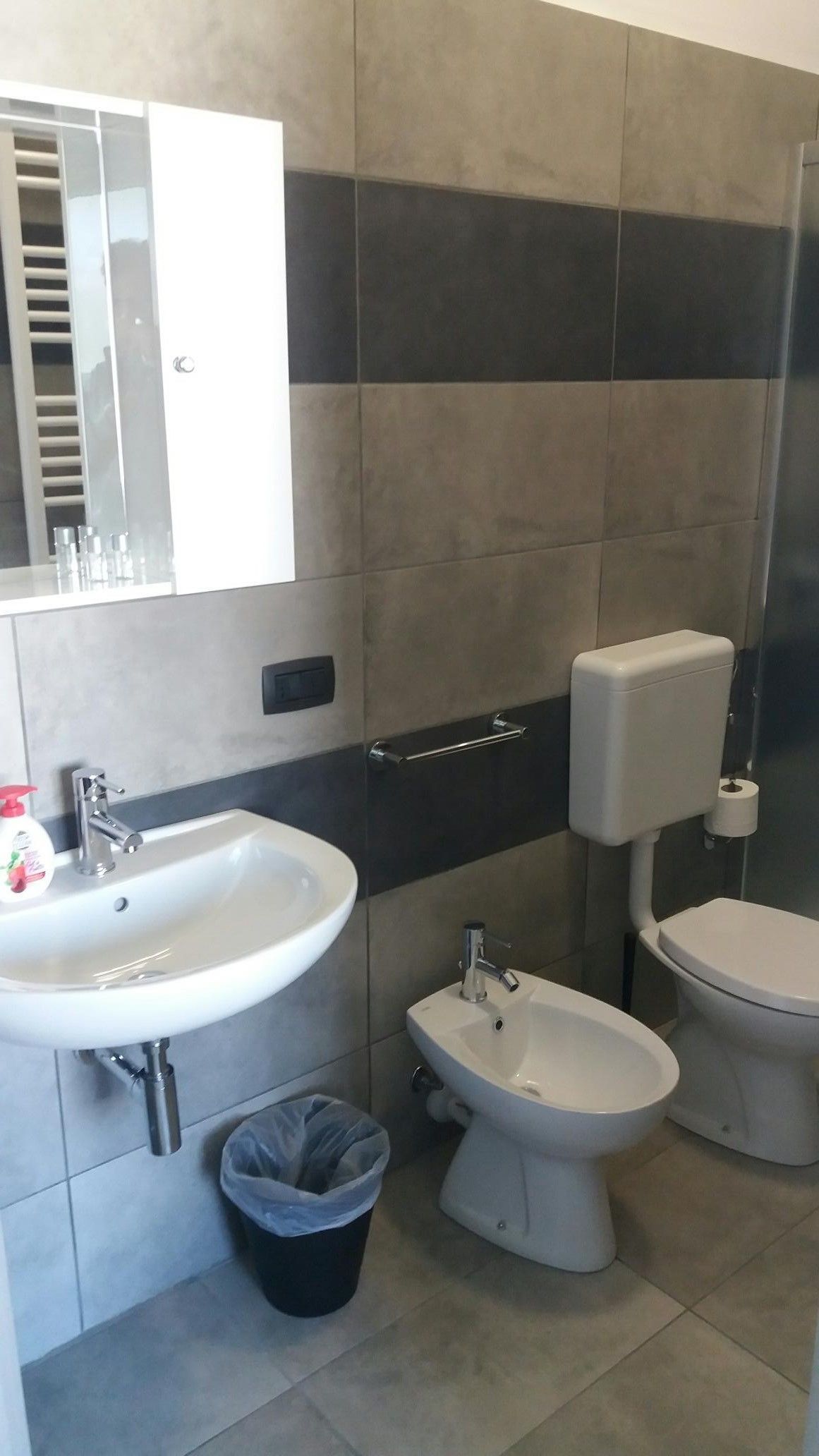 A bathroom with a sink, bidet, toilet, and a trash bin.