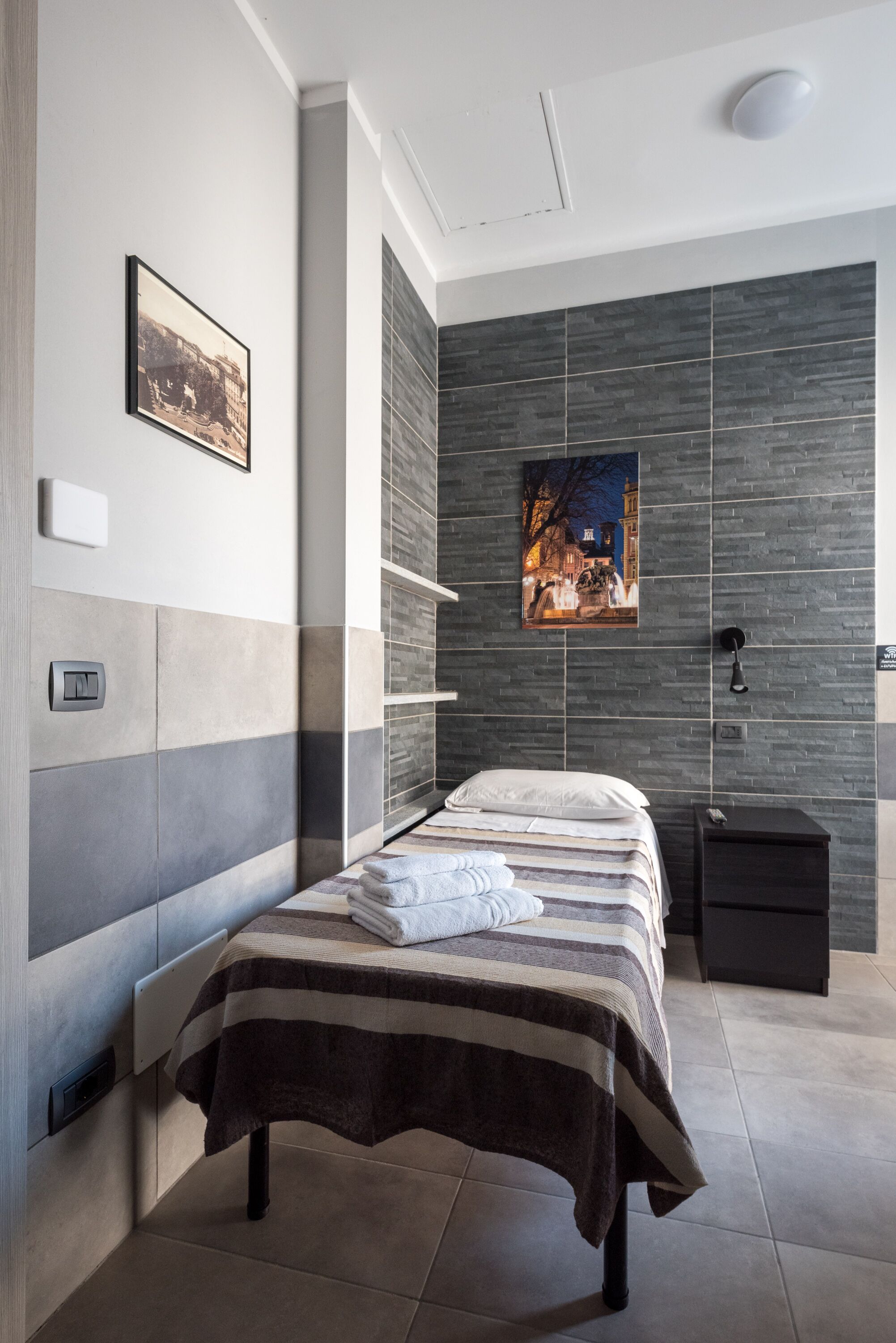 Una camera da letto moderna con un letto, un comodino, una mensola a muro e un quadro con vista sulla città.