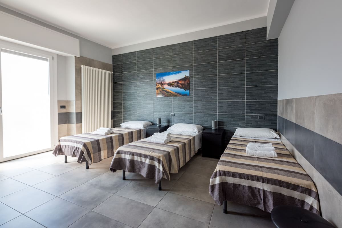 Habitación de hotel con tres camas, un ventanal grande y vista a un lago.