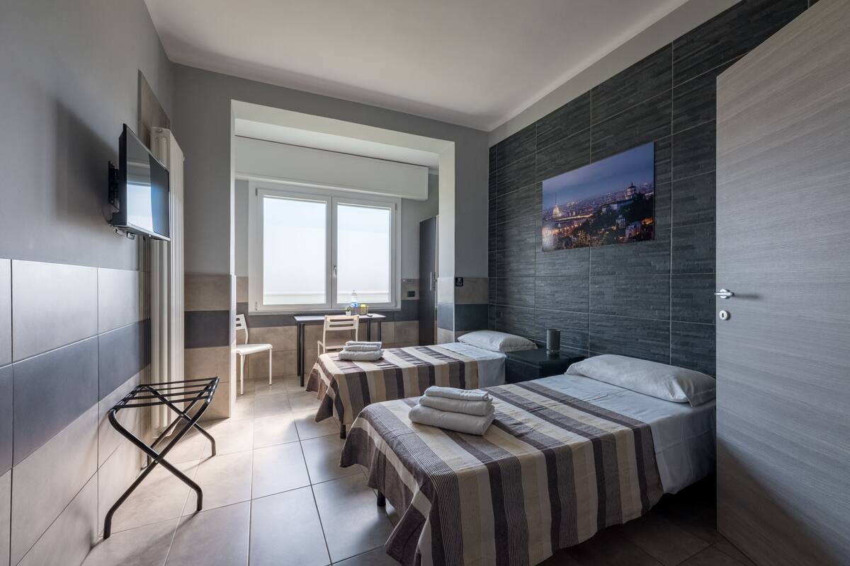 Una habitación de hotel moderna con dos camas, televisión, vista panorámica de la ciudad y una ventana.