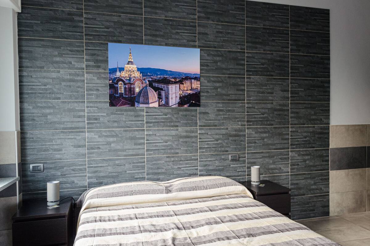 Un dormitorio moderno con una cama grande, una mesita de noche y un cuadro colgado en la pared que muestra un paisaje urbano.