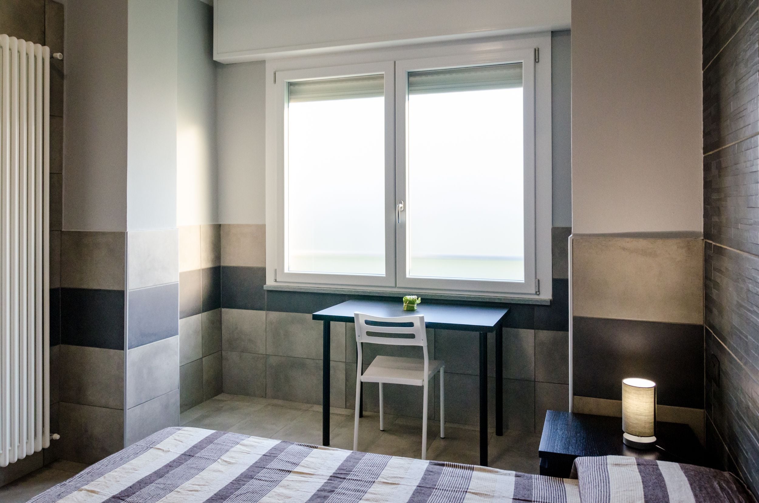 Une petite pièce moderne, dotée d’une fenêtre, d’un bureau, d’une chaise et d’une lampe.